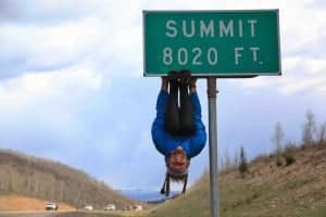 Rob Greenfield hangs from a summit elevation sign. Photo by Brent Martin